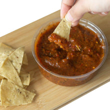 Load image into Gallery viewer, A hand dipping Corn Nacho Chips in a container of Mad Mexican Salsa Morita