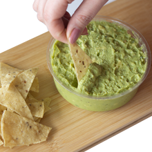 Load image into Gallery viewer, A hand dipping nacho chips in Chunky Guacamole with a side of corn nacho chips
