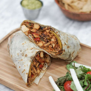 Chicken Fajita Burrito with a side salad on a wooden board. A bowl of corn nacho chips and salsa verde in the background