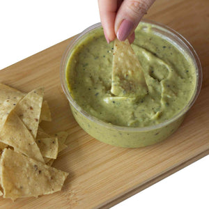 A hand dipping a nacho in Mad Mexican Roasted Tomatillo and Avocado Salsa
