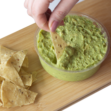 Load image into Gallery viewer, A hand dipping nacho chips in Chunky Guacamole with a side of corn nacho chips
