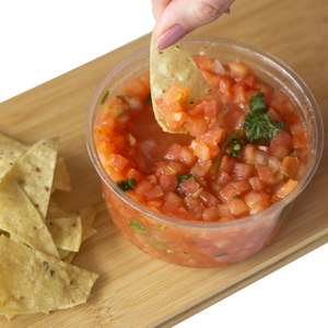 A hand dipping Corn Nacho Chips in a container of Pico de Gallo